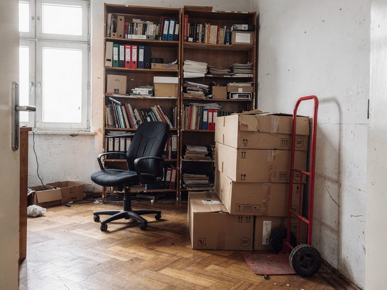 Zimmer in Stuttgart vor der Entrümpelung: volle Bücherregale, gestapelte Kartons und eine rote Sackkarre