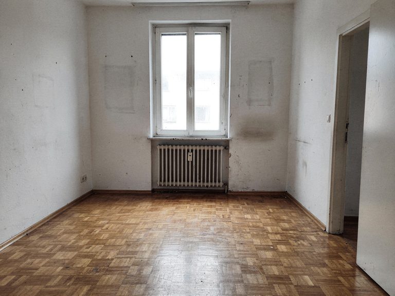 Dasselbe Zimmer nach der Entrümpelung: leer, gekehrt, nur Parkett und Fenster