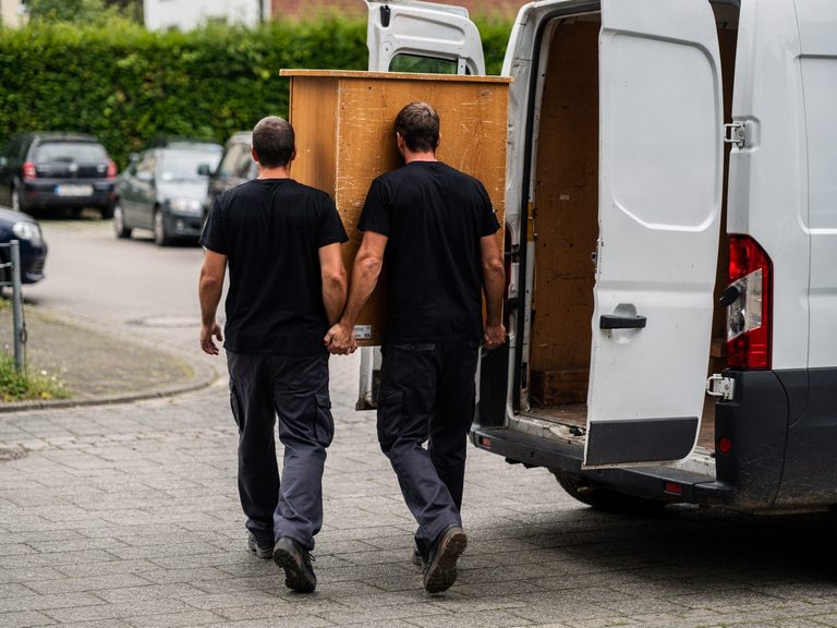 Zwei Mitarbeiter tragen einen Holzschrank zum Transporter