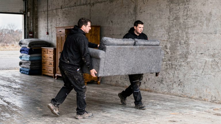 Zwei Mitarbeiter tragen gemeinsam ein Sofa durch die Halle
