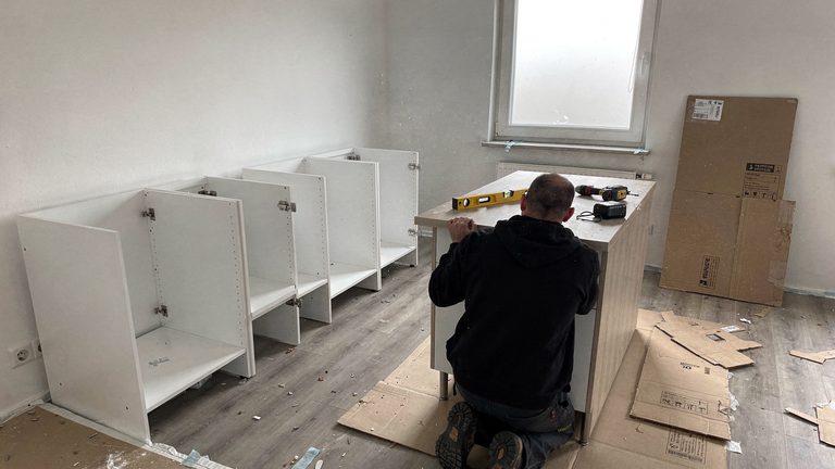 Monteur richtet einen Küchenunterschrank aus, daneben Werkzeug und Schrankteile